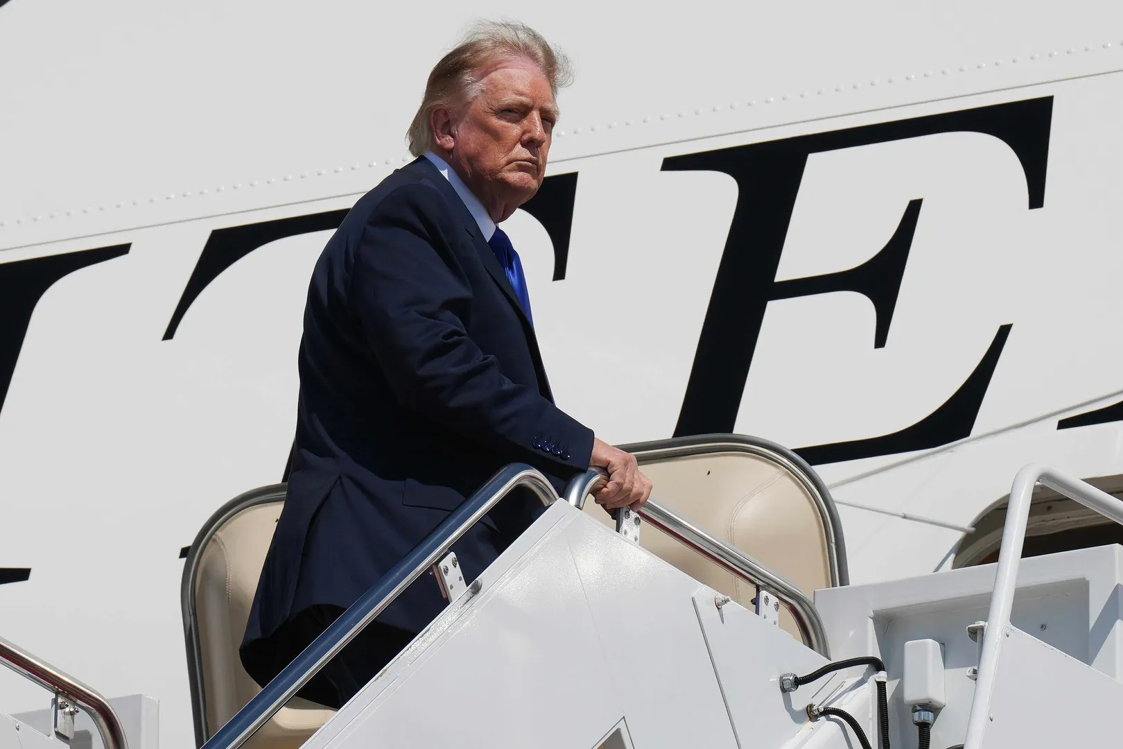 Donald Trump climbs aircraft stairs beside the doorway of a large white jet.