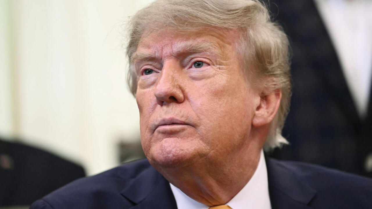Close-up portrait of a suited man with blond hair looking upward, with blurred people in background.