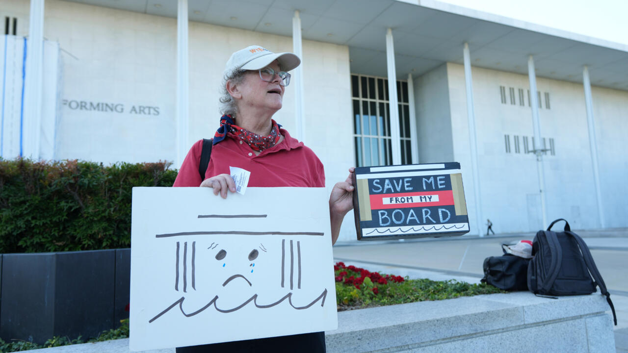 Person holding hand-drawn protest signs outside a performing arts building.