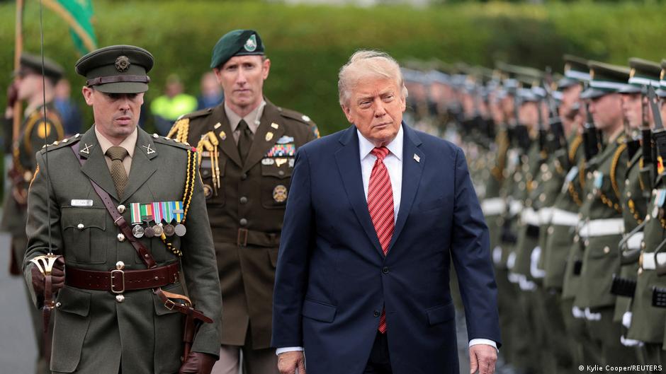 Donald Trump walks beside decorated military officers during a formal outdoor ceremony.