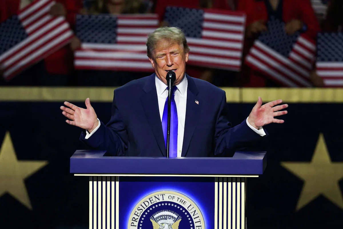 Donald Trump speaks at a podium with American flags behind him, gesturing with both hands.