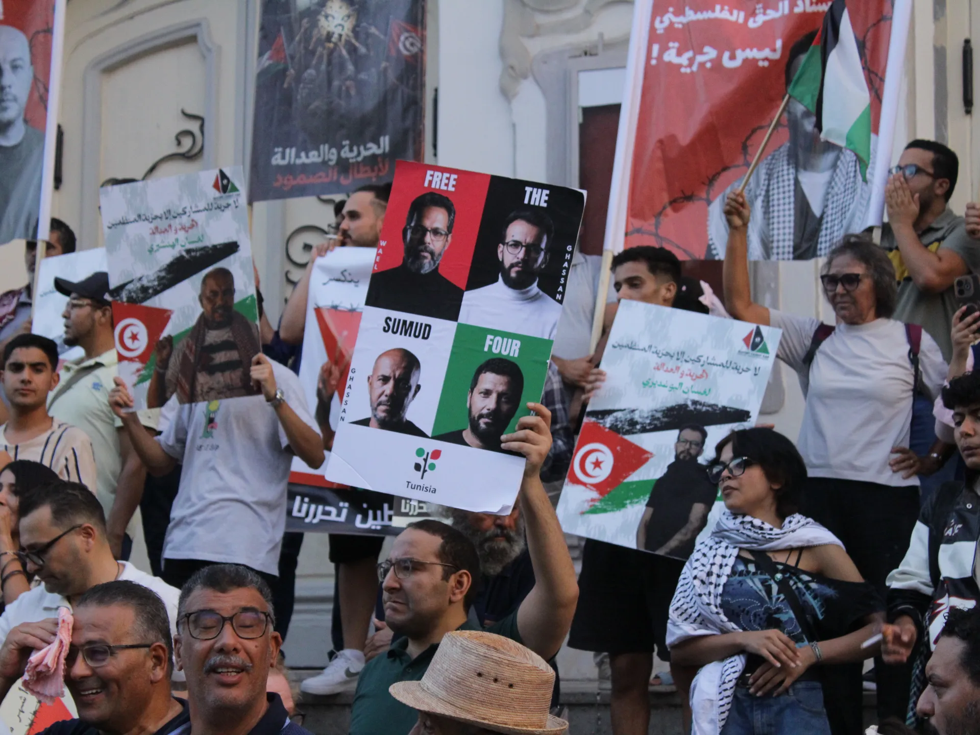 Protesters hold signs, Palestinian flags, and a poster calling for four activists' release.