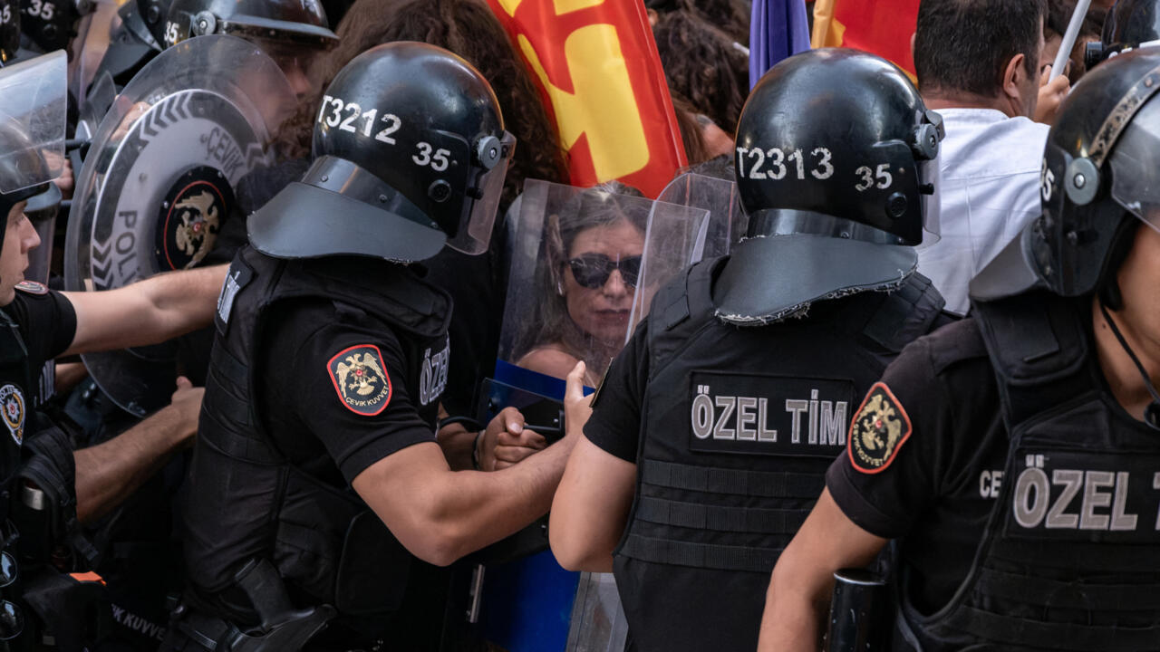 Turkish riot police in helmets and shields confront protesters amid a crowded demonstration.