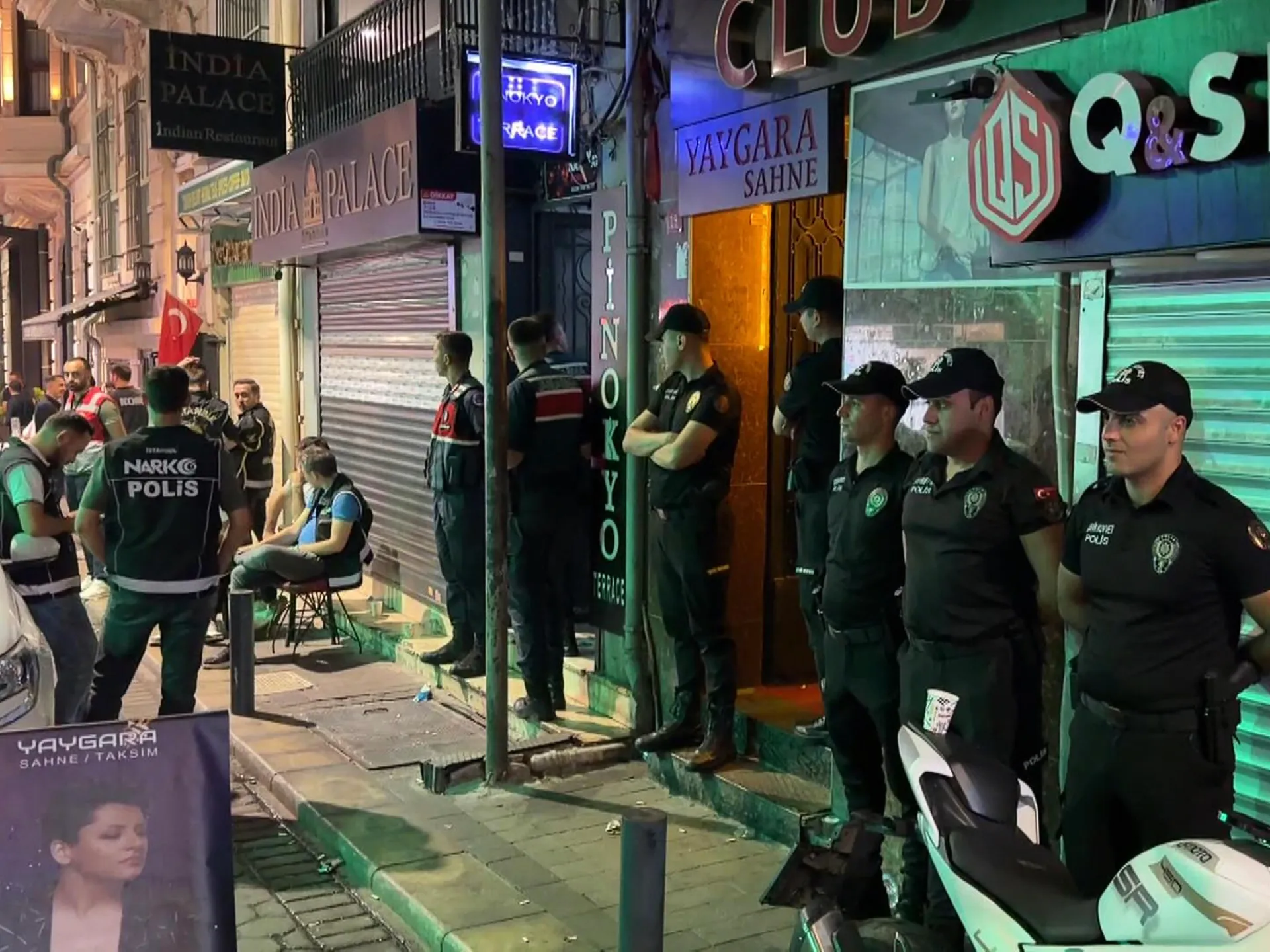 Uniformed Turkish police officers stand outside nightlife venues as bystanders gather on the sidewalk.