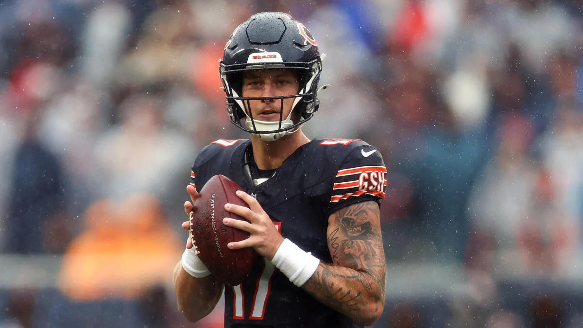 Chicago Bears quarterback holds a football during practice in a black uniform and helmet as rain falls.
