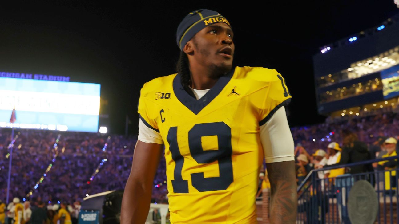 Michigan football player wearing number 19 walks past a nighttime stadium crowd.
