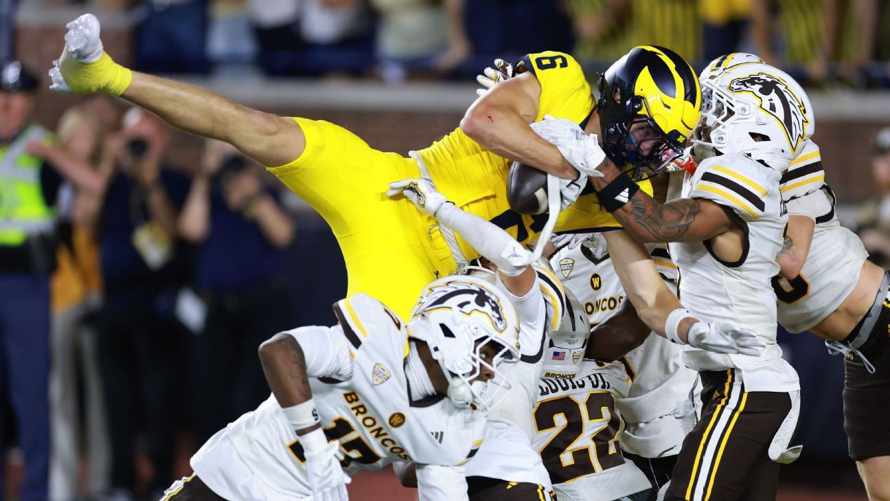 Michigan player in yellow uniform is tackled by Western Michigan defenders in white uniforms.