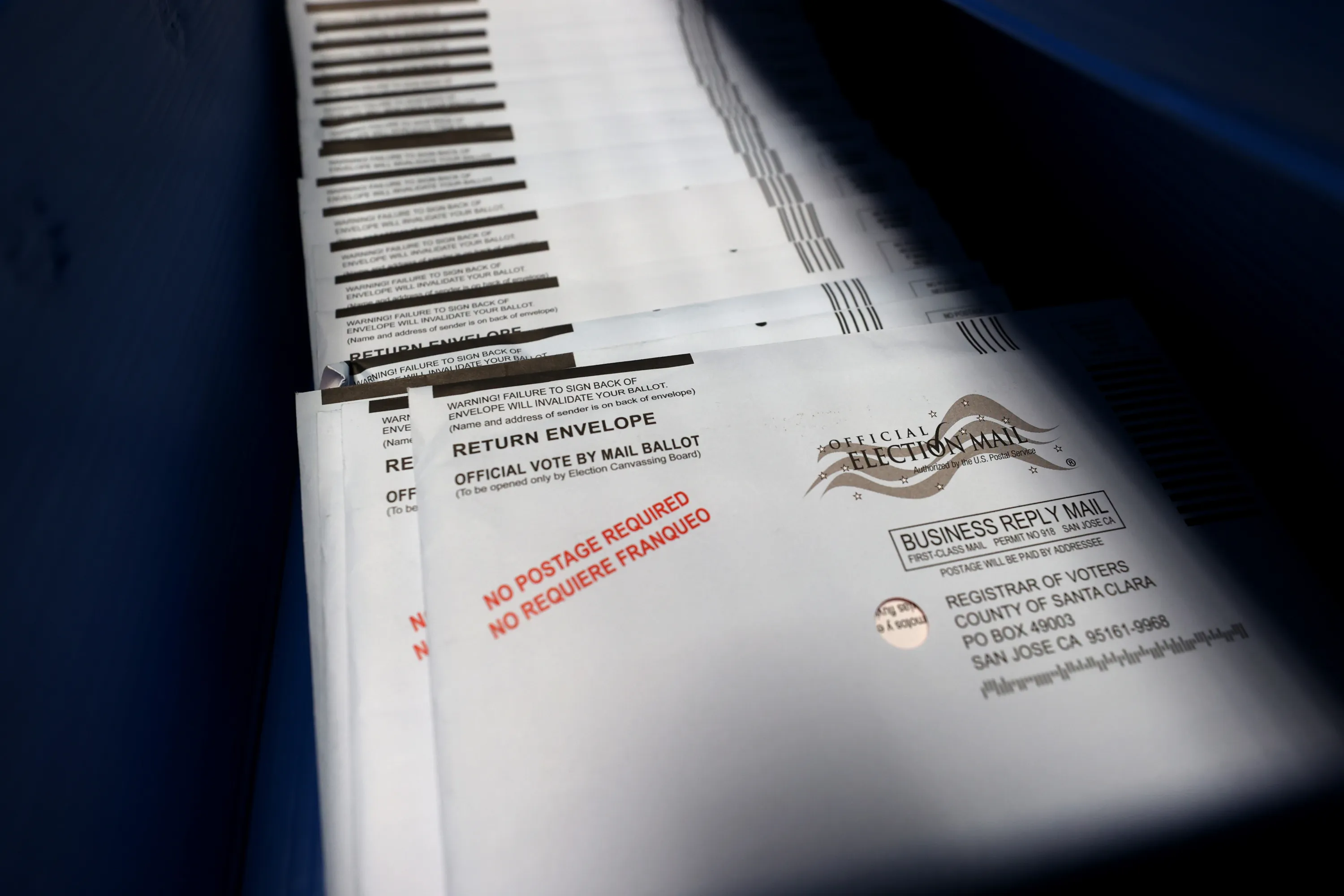 Stack of official election mail ballot return envelopes resting on a dark surface.