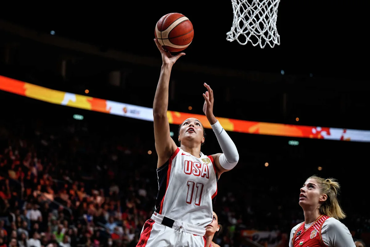 Basketball player in USA jersey reaches toward the hoop for a layup during a game.