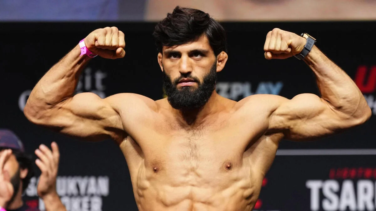 Bearded shirtless fighter flexes both arms during a weigh-in pose before a UFC event