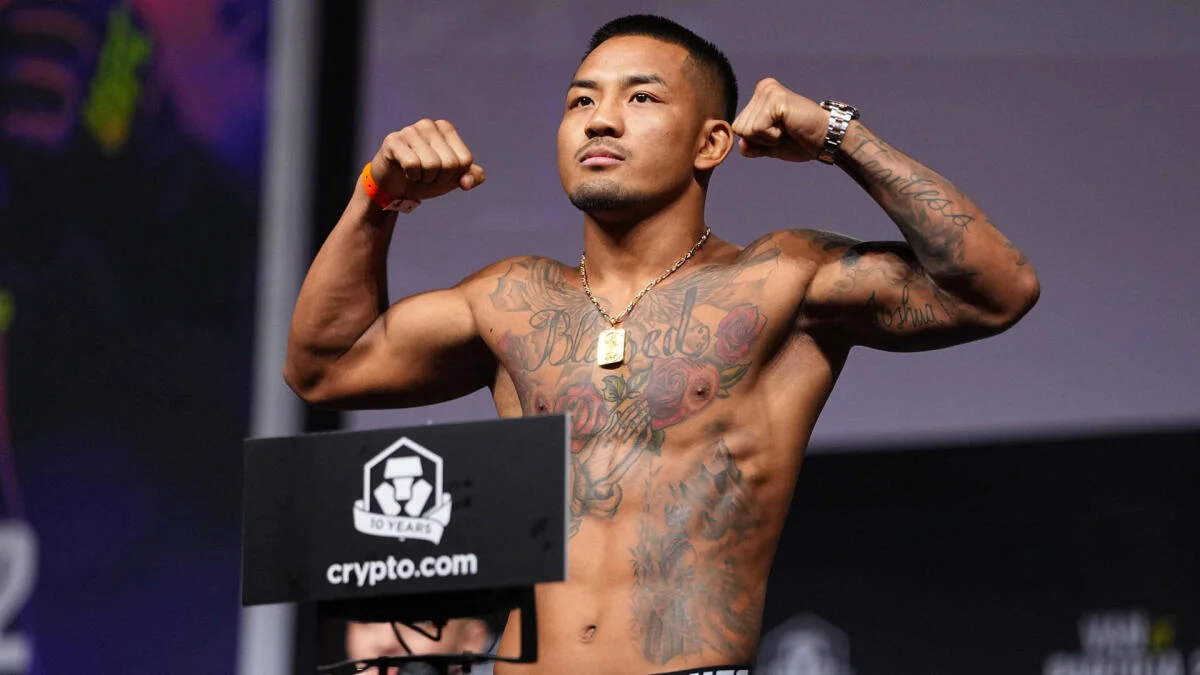 Tattooed male fighter flexes both arms beside a crypto.com sign during a weigh-in.