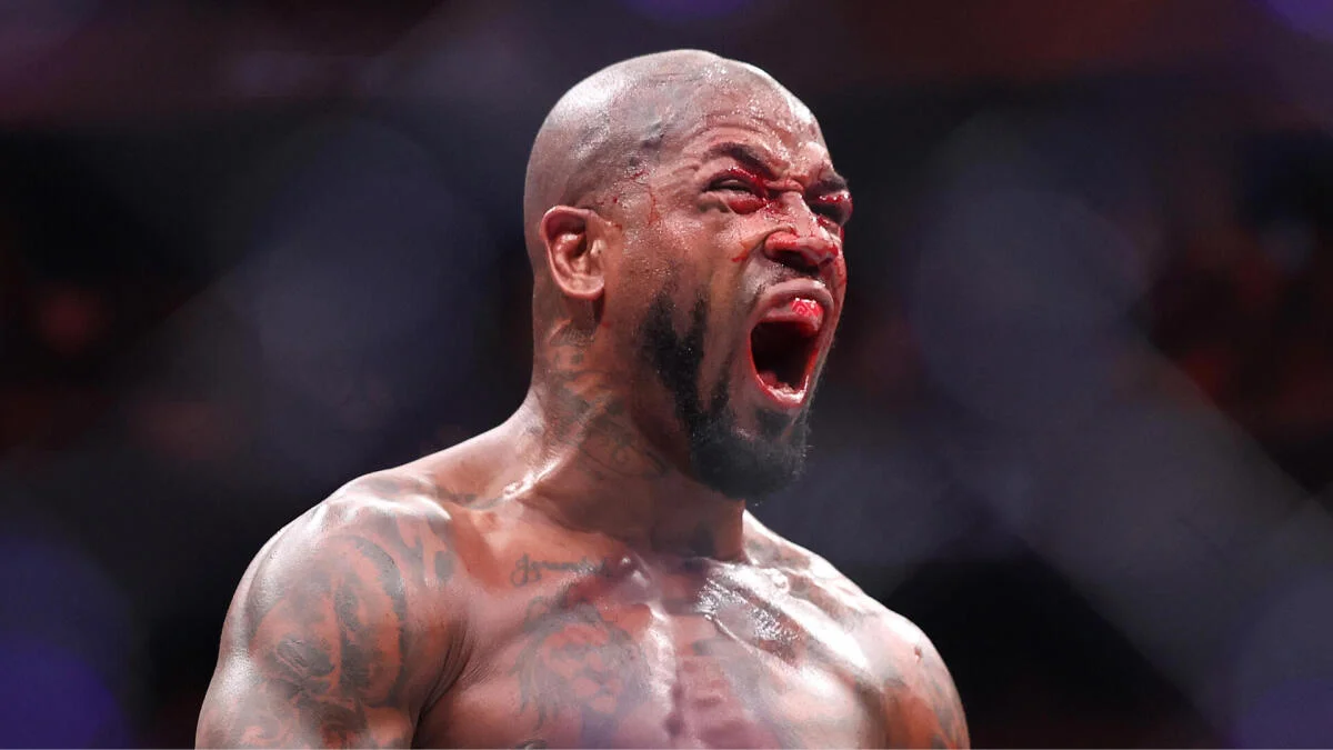 Bald, tattooed fighter shouts with a bloodied face under arena lights.