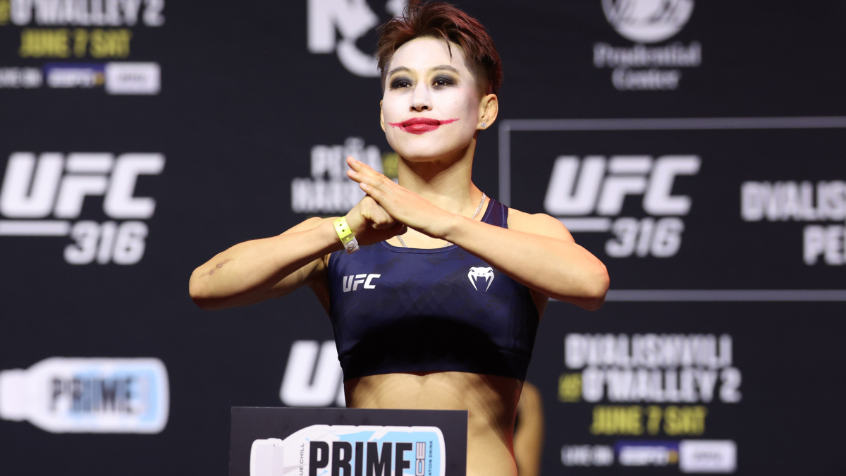 A female fighter poses with crossed hands and red face paint at a UFC weigh-in event.