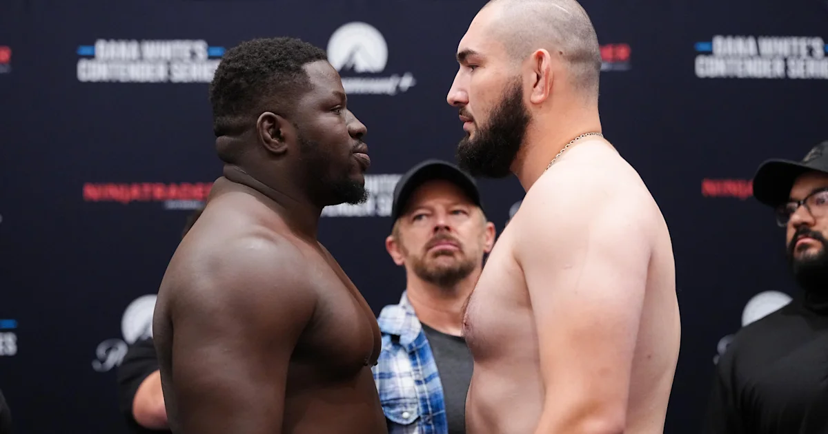 Two shirtless heavyweight fighters face off at a UFC event, with staff members behind them.