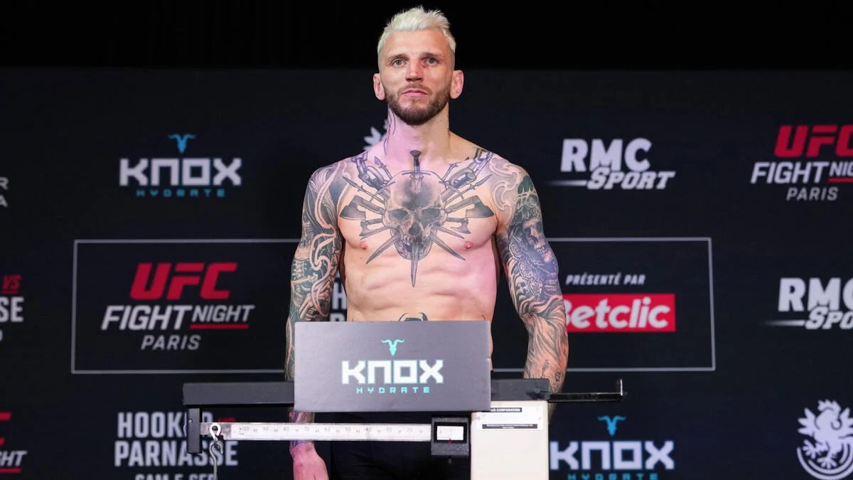 Tattooed male fighter stands shirtless on a weigh-in scale before a UFC event.