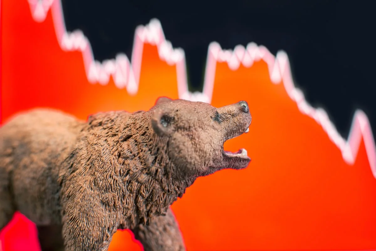 Bear figurine with open mouth against a sharply declining red stock market chart