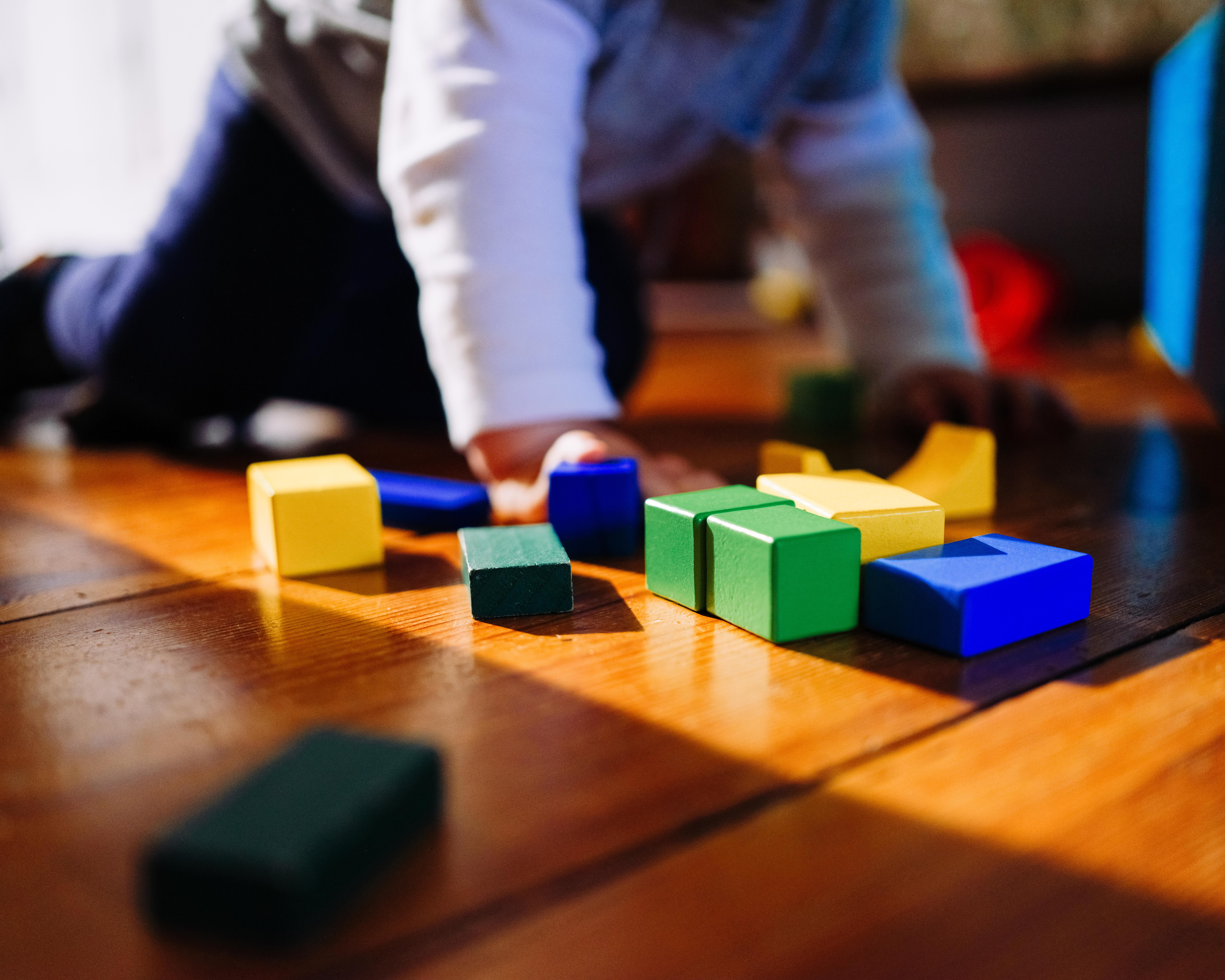 Blurred adult arranging colorful wooden blocks on a wooden table