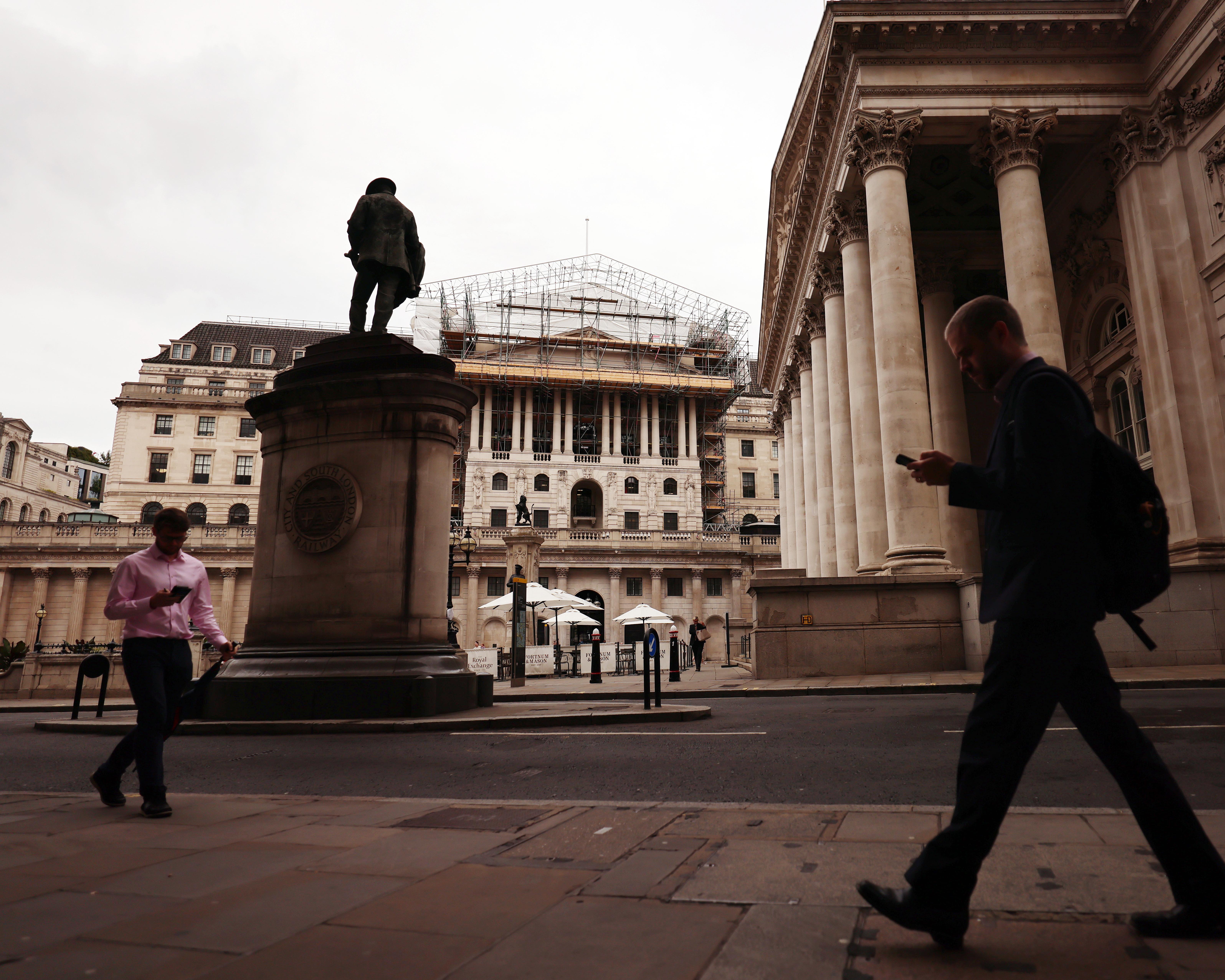 Pedestrians walk past grand columns, a statue, and scaffolding in a city financial district.
