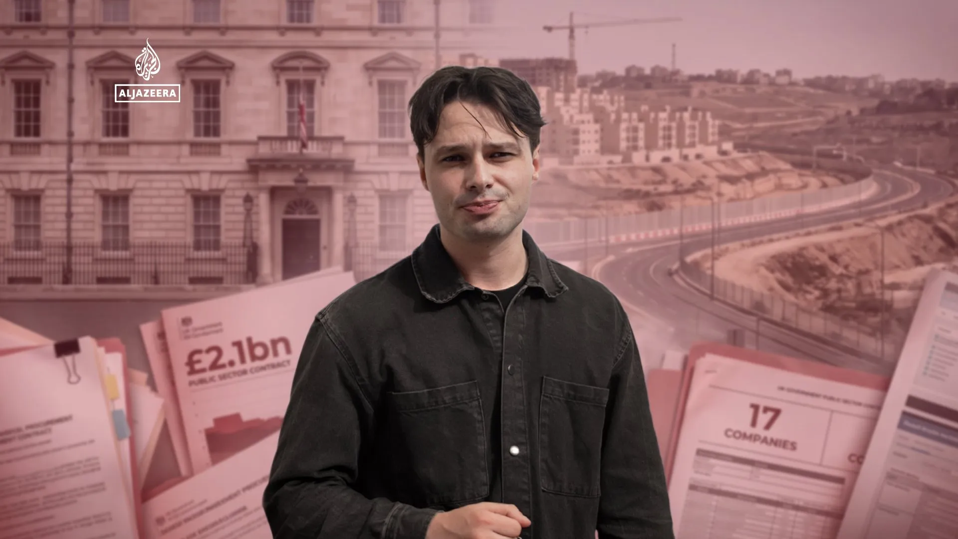 Man in black shirt stands before a news graphic showing documents, roads, buildings and Al Jazeera branding.