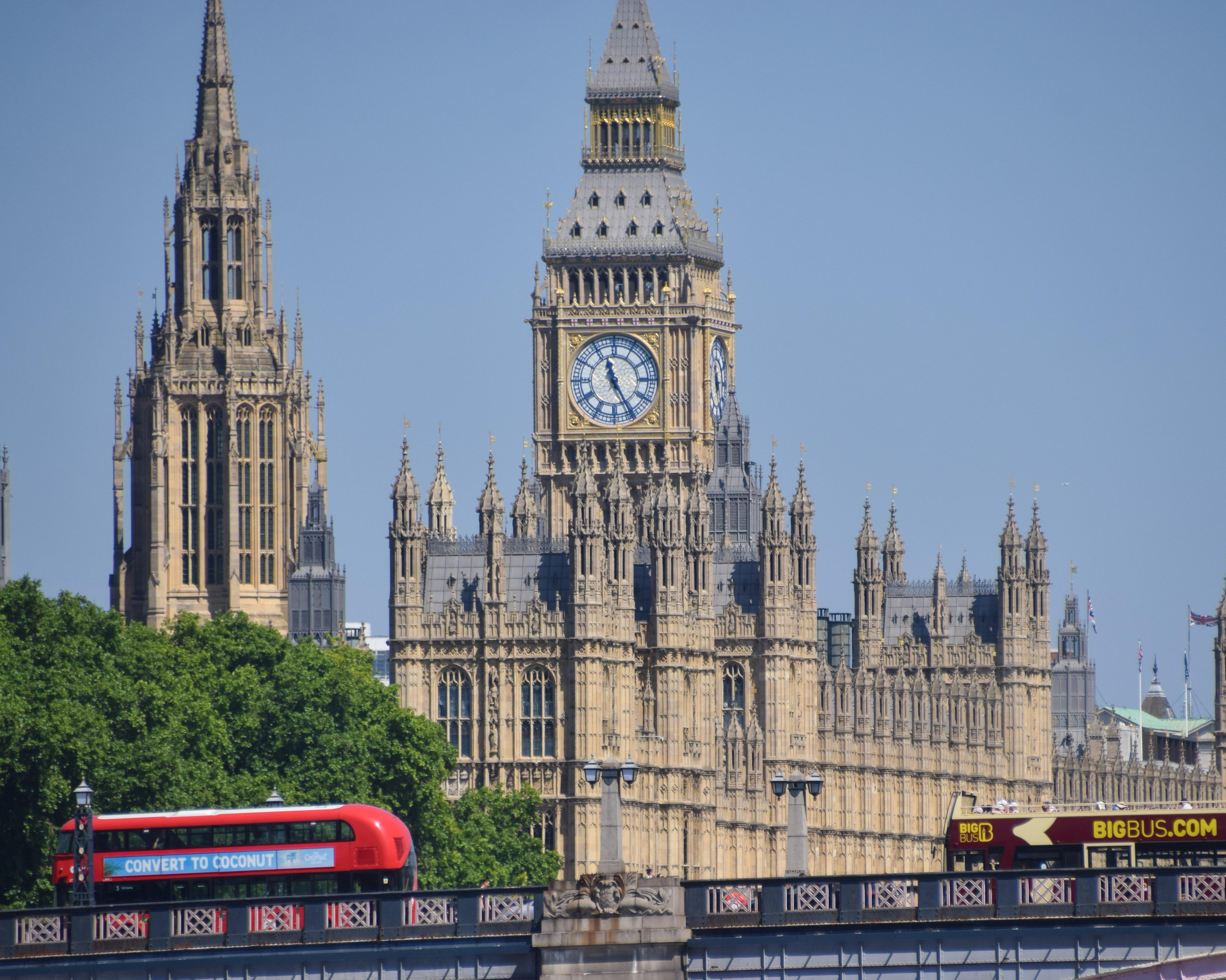 London's Houses of Parliament and Big Ben viewed behind red double-decker buses on Westminster Bridge.