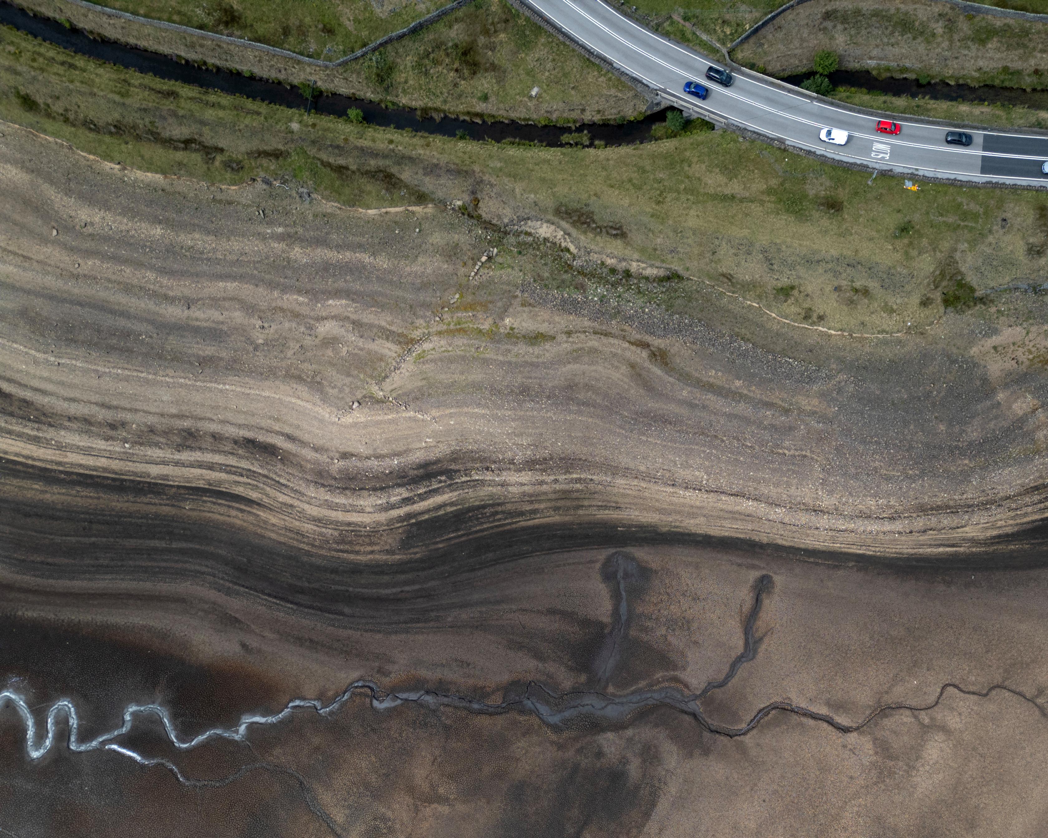 Aerial view of a road crossing a narrow stream beside dry, layered terrain