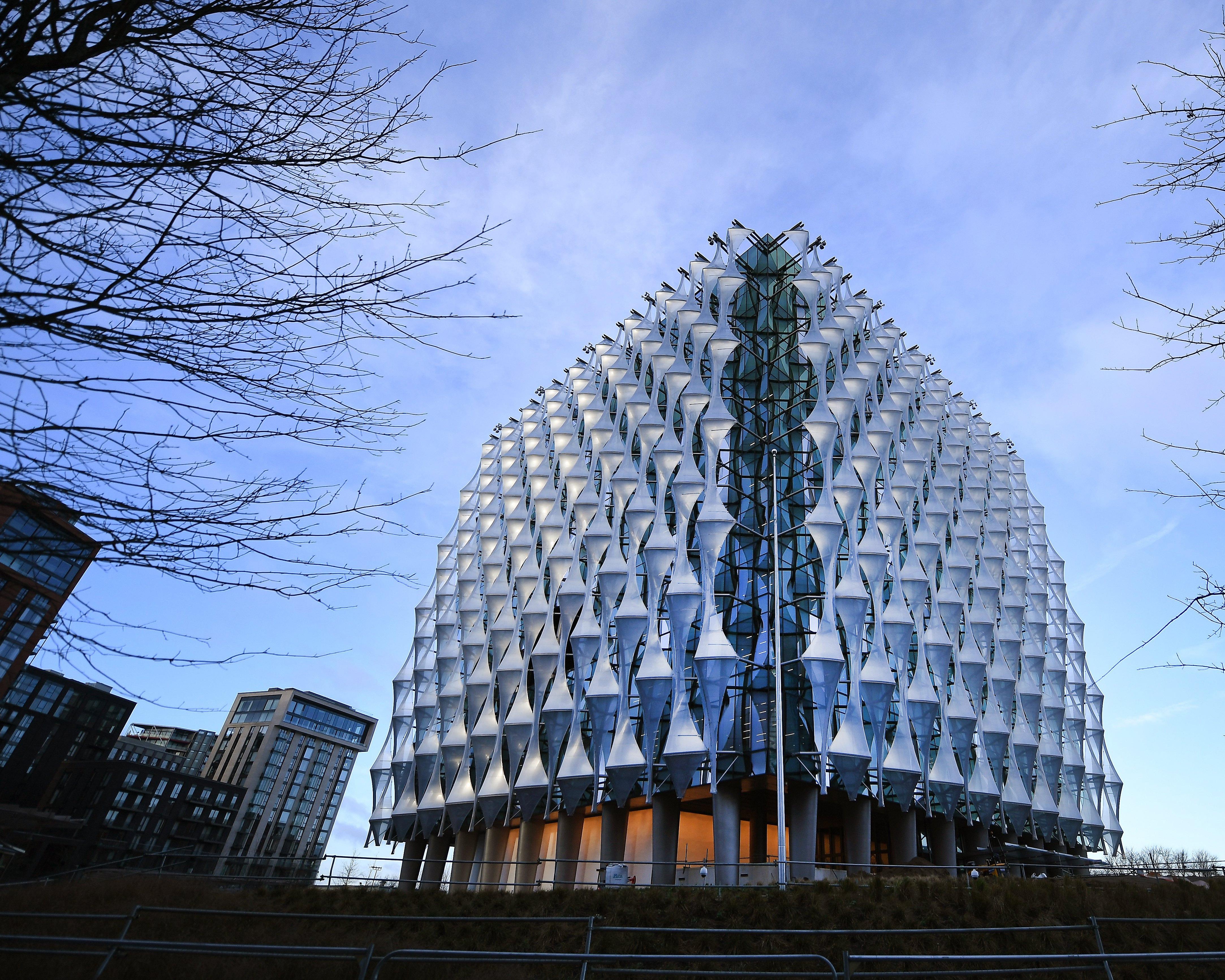 Modern glass building with sculptural white facade framed by bare tree branches beneath a blue sky