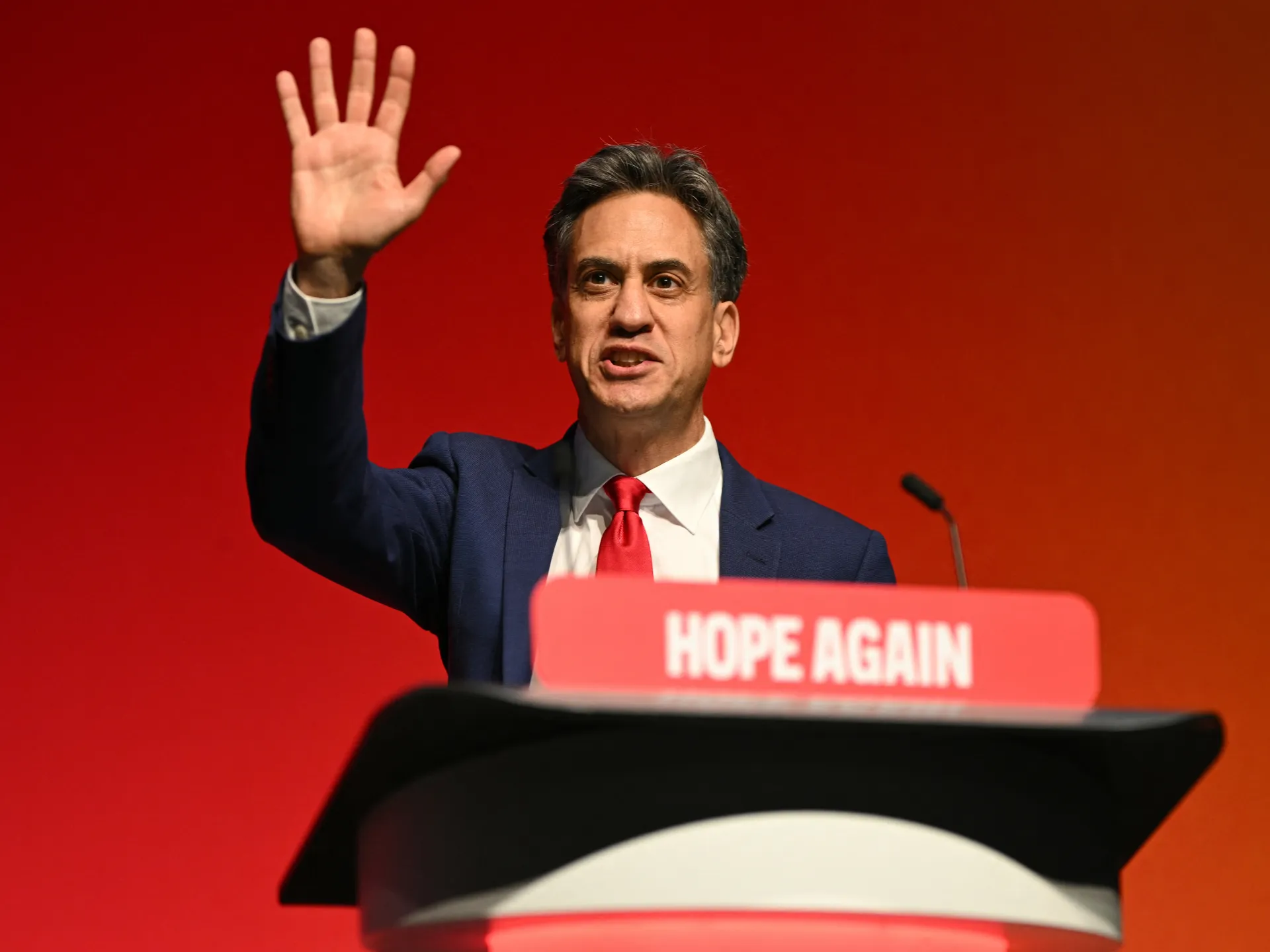 A suited man raises his hand behind a lectern with a red “HOPE AGAIN” sign.