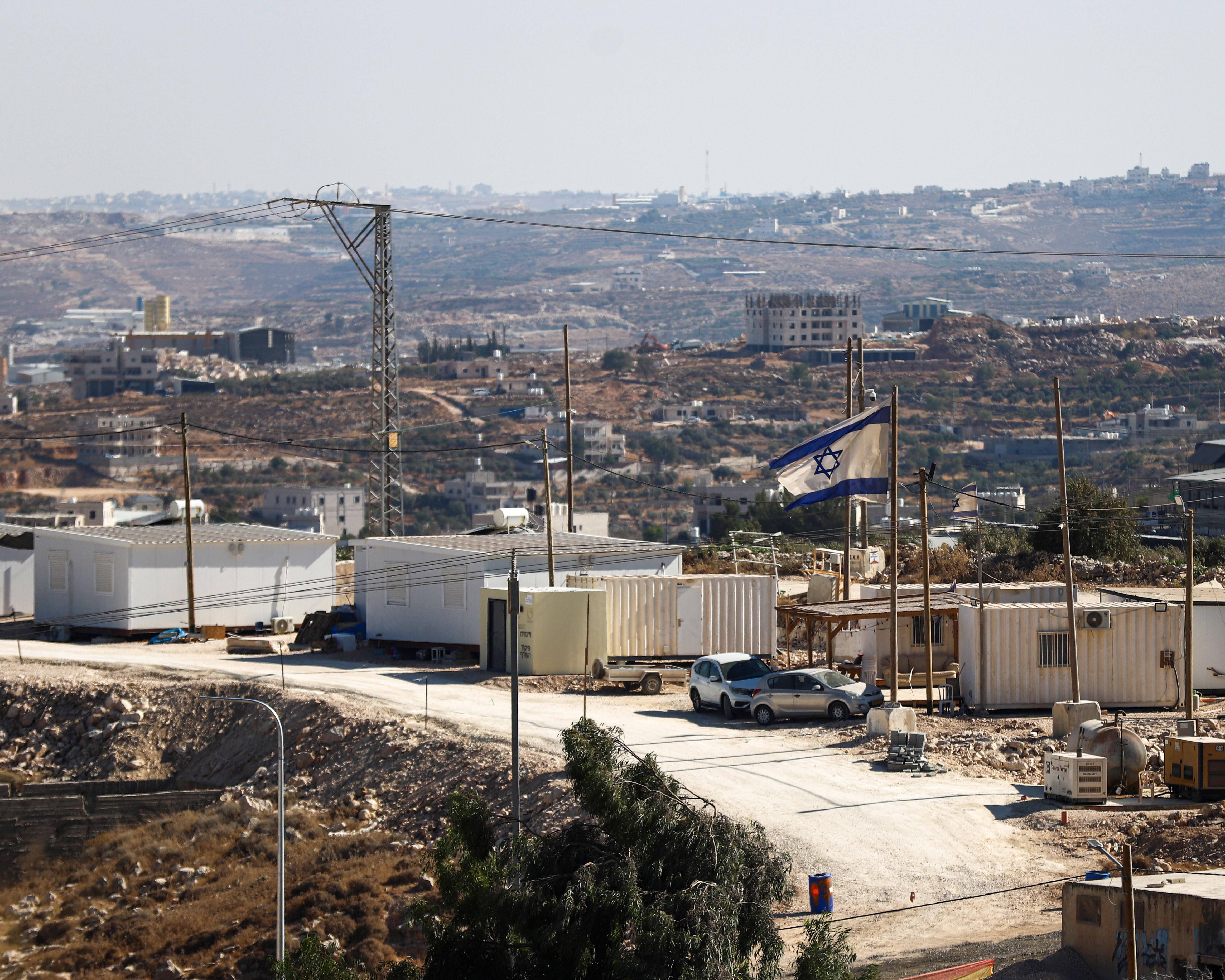 Israeli flag flying above temporary buildings and rugged, densely settled hills with utility wires