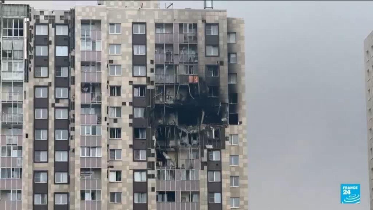 Apartment building facade with extensive blast damage, shattered windows, and exposed rooms.