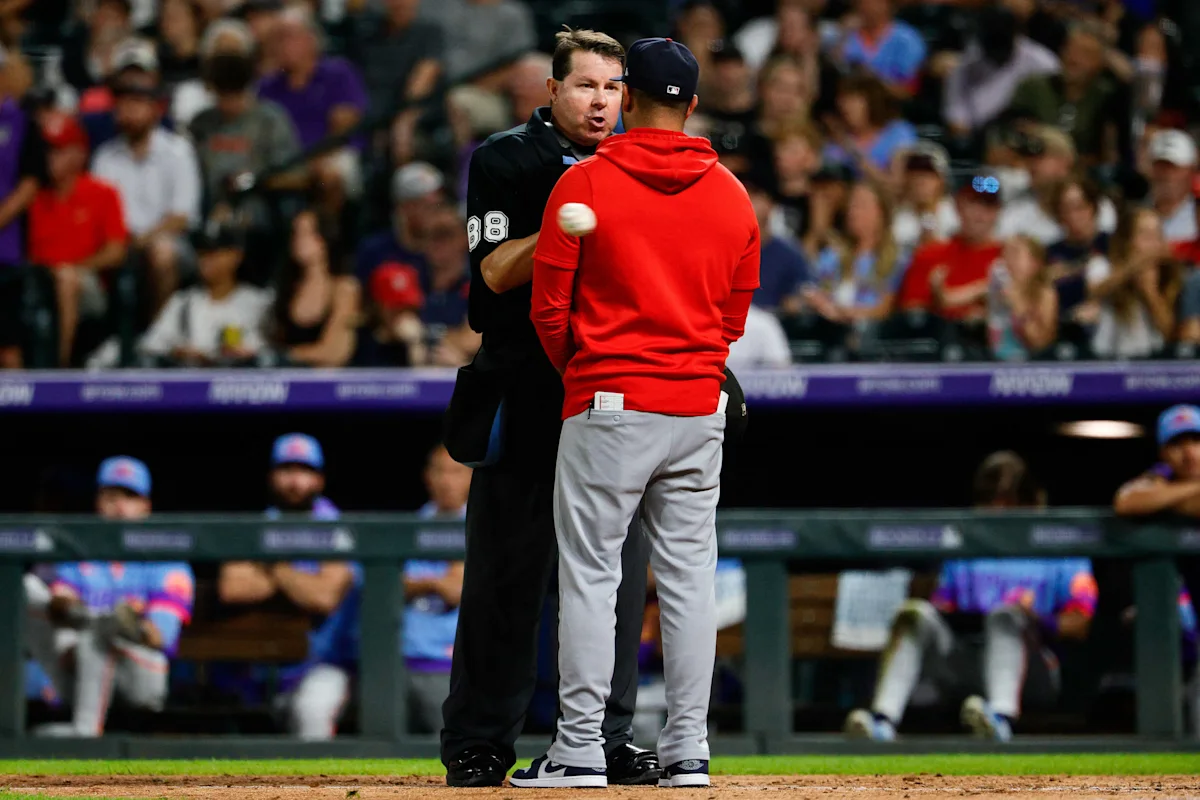 Baseball umpire and manager in red hoodie stand facing each other on the field