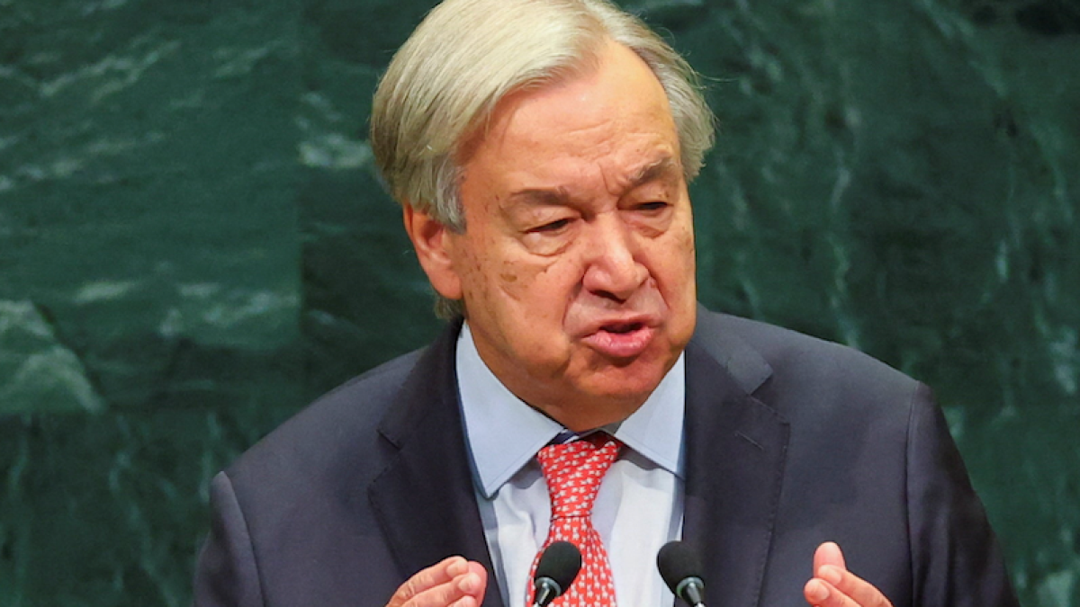 Gray-haired man in a suit and red tie speaking at a podium with microphones