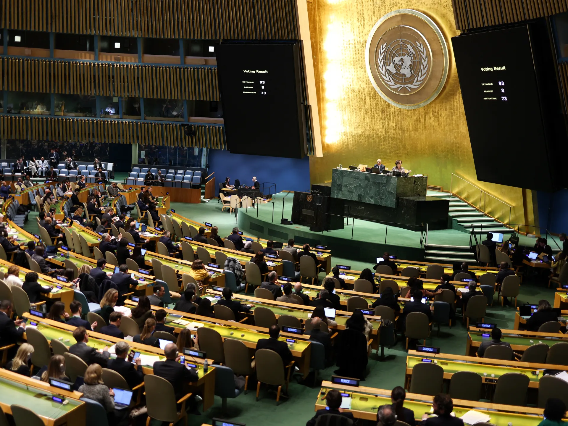 Delegates sit in the UN General Assembly hall as large screens display voting results.