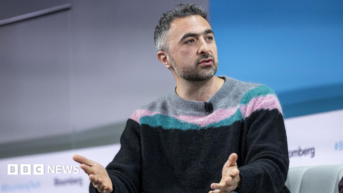 Man in striped sweater gestures while speaking during a panel discussion.