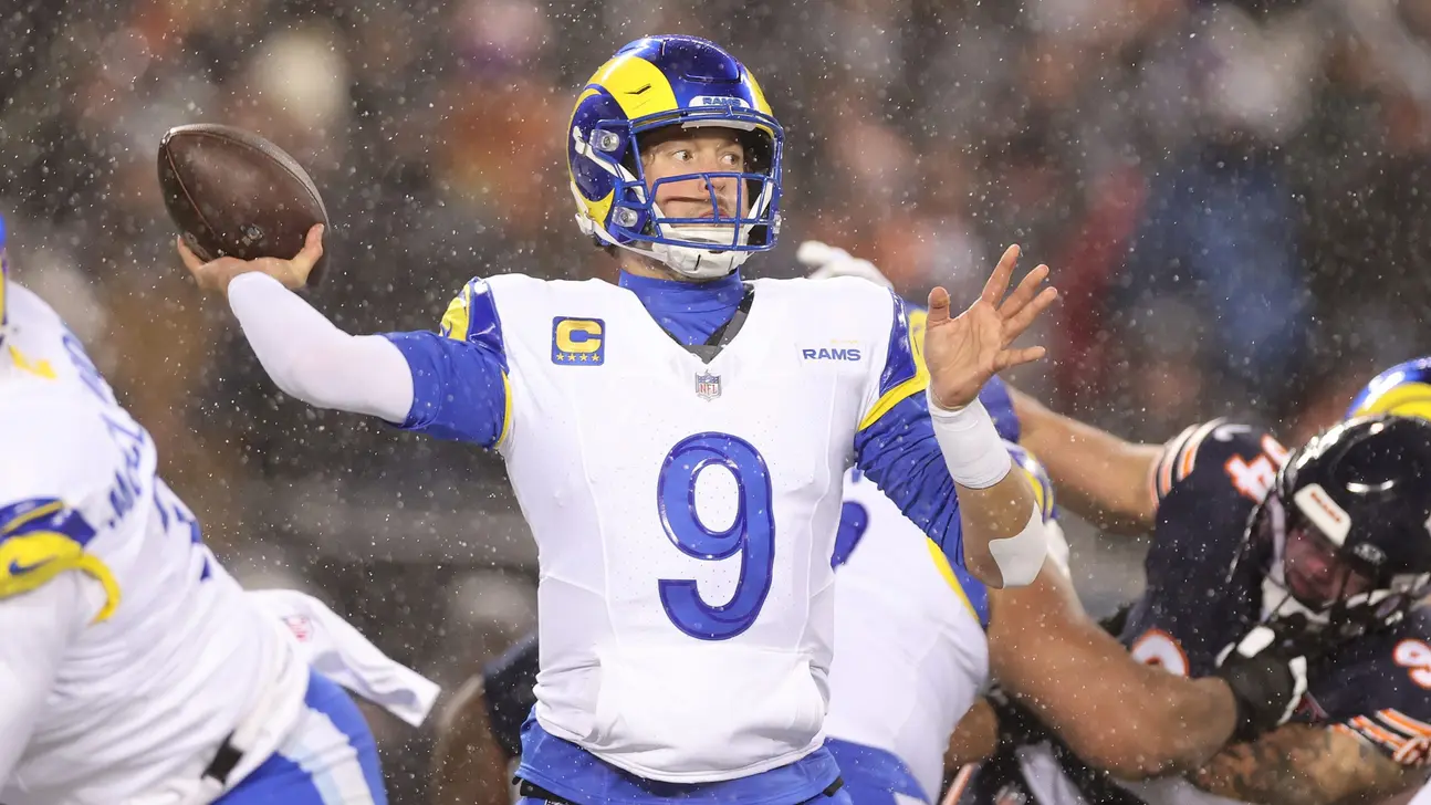 Rams quarterback throws a football during a snowy NFL game as defenders close in