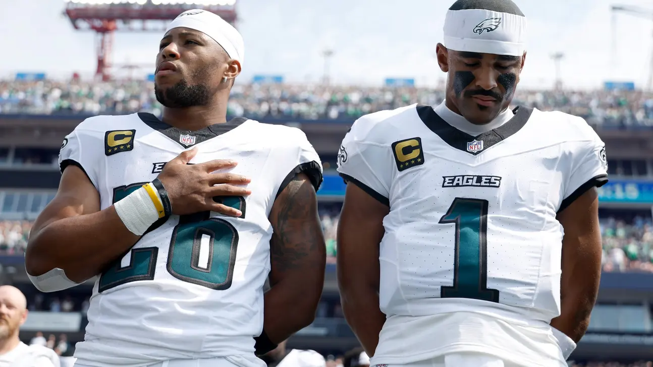 Two Philadelphia Eagles players in white uniforms stand on the field, one with a hand on his chest.