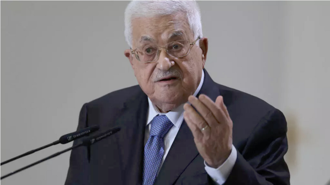 Older man in suit and glasses gestures while speaking into microphones at a podium