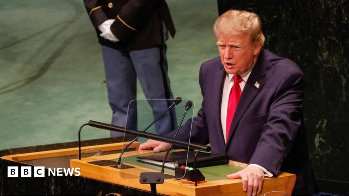 Donald Trump speaks at a lectern, with microphones and a person standing behind him.