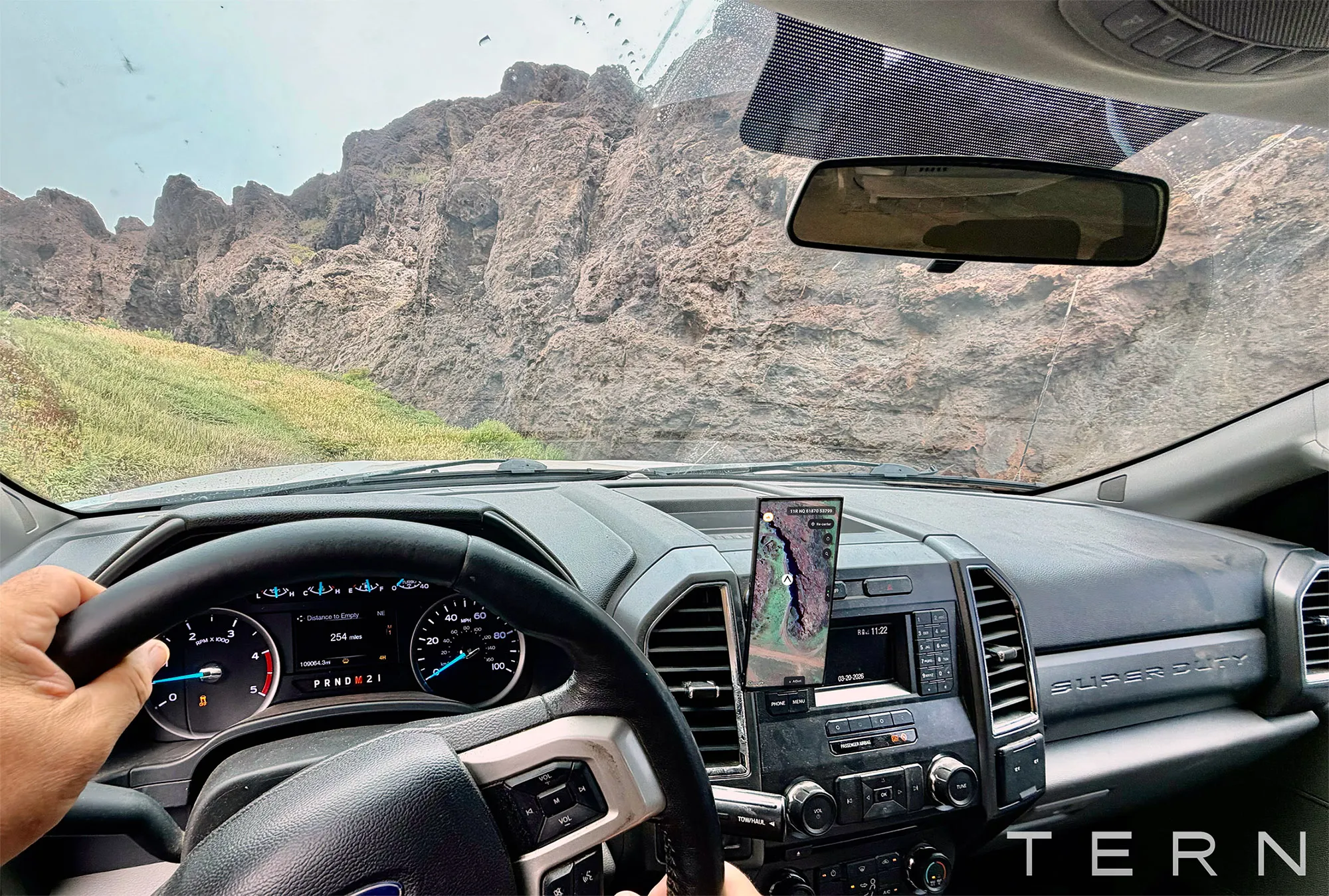 Driver views rugged volcanic cliffs from inside a Ford truck using a mounted navigation phone