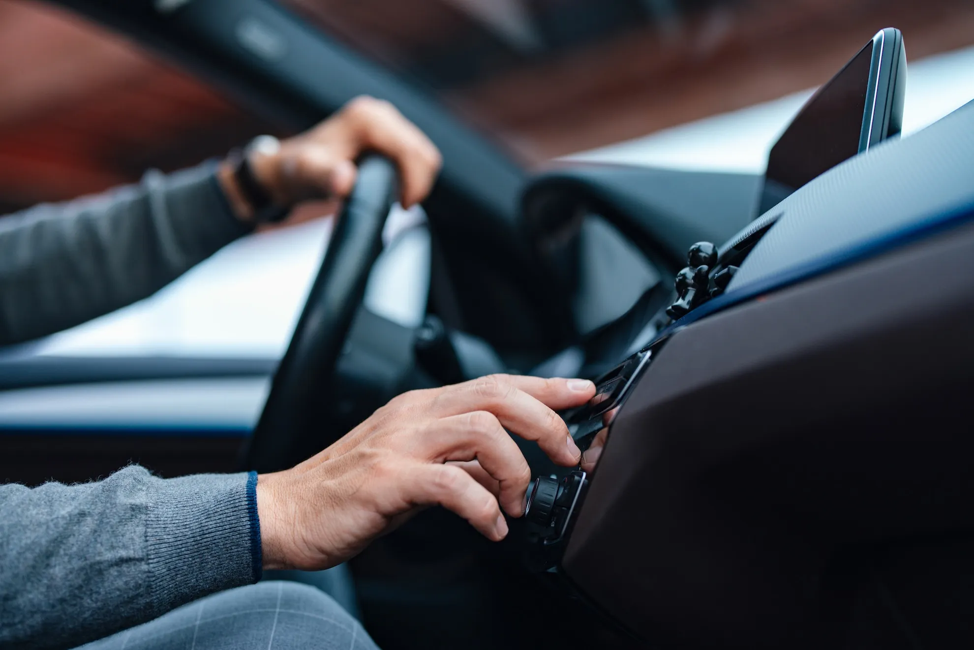 Driver’s hand adjusts controls on a car dashboard beside the steering wheel