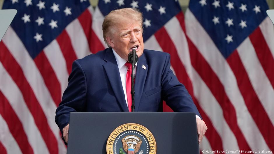 Donald Trump speaks at a podium before a backdrop of American flags.
