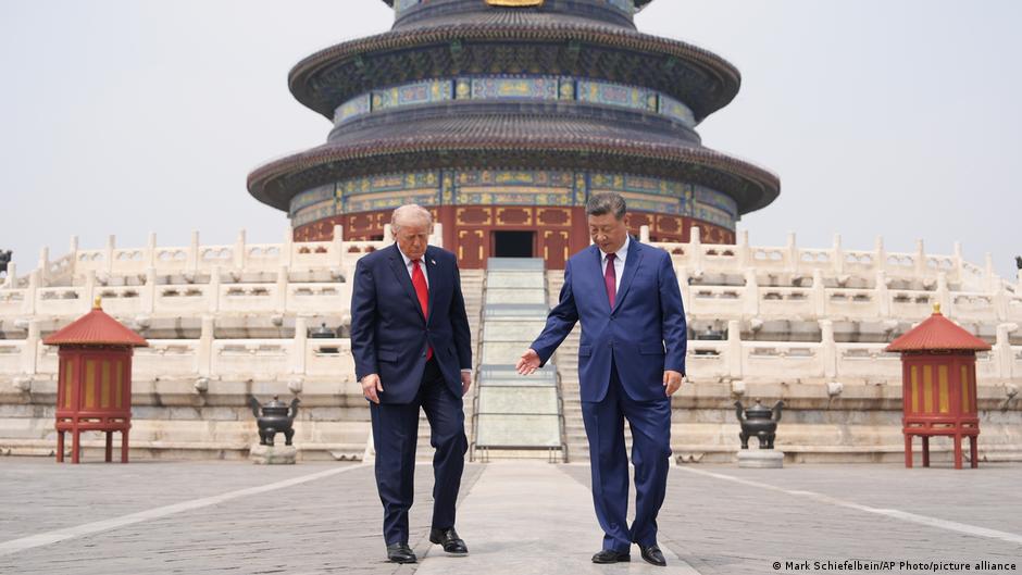 Two suited men walk across a courtyard before an ornate multi-tiered temple.
