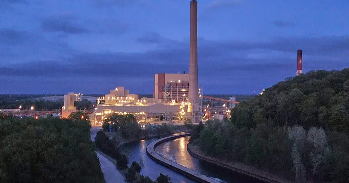 Illuminated industrial power plant with tall smokestacks beside a canal at dusk