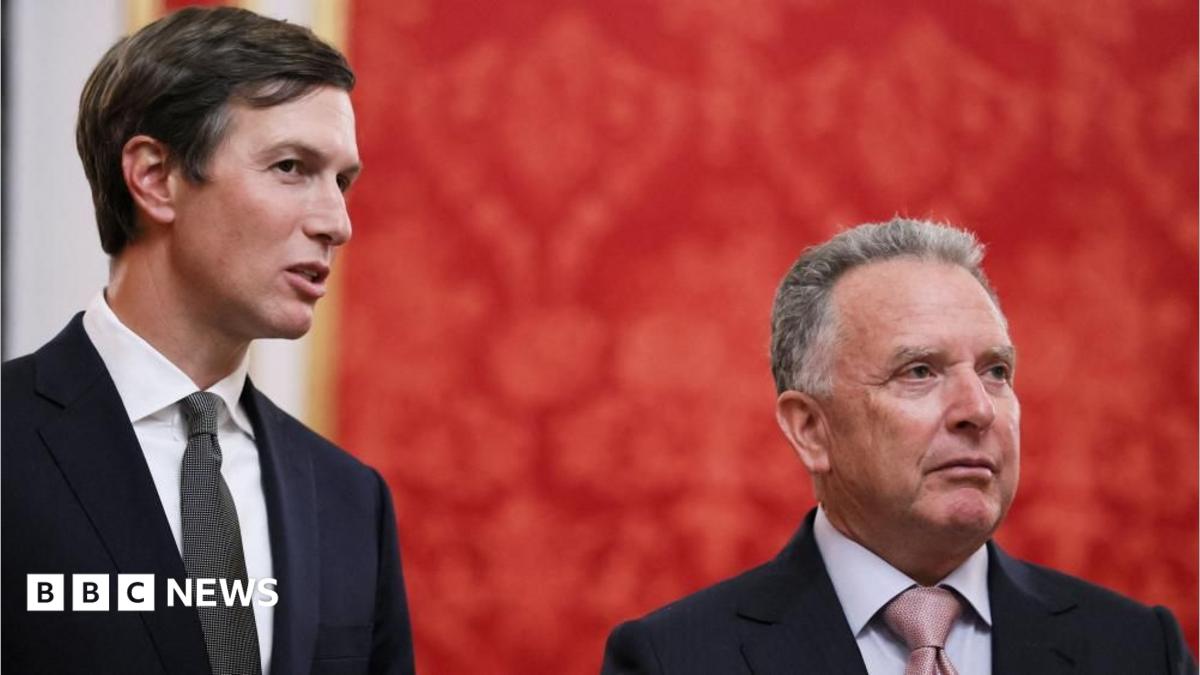 Two suited men stand before a red backdrop, with a BBC News logo at lower left.