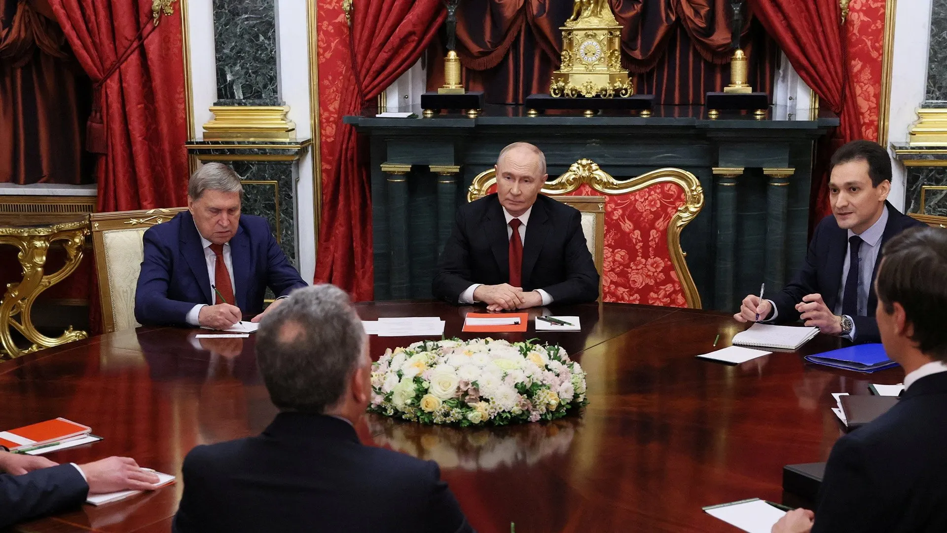 Officials sit around a polished table during a formal meeting in an ornate room.
