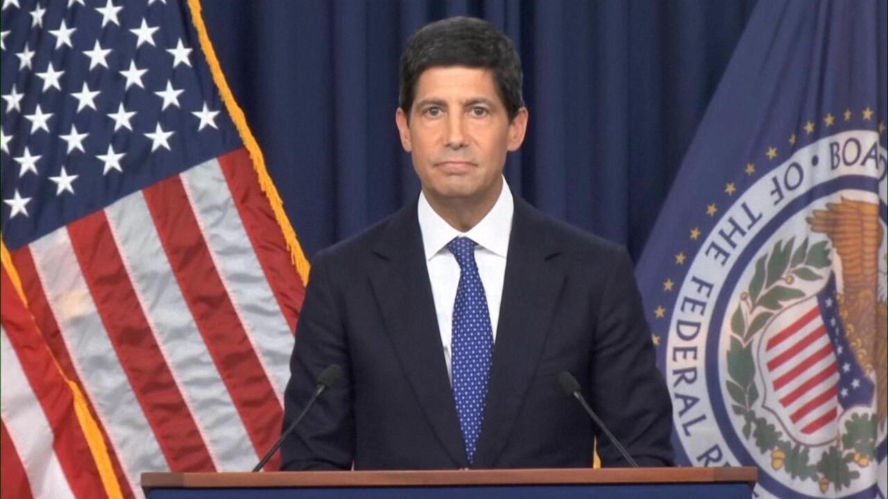 Federal Reserve official standing at podium between U.S. and Federal Reserve flags