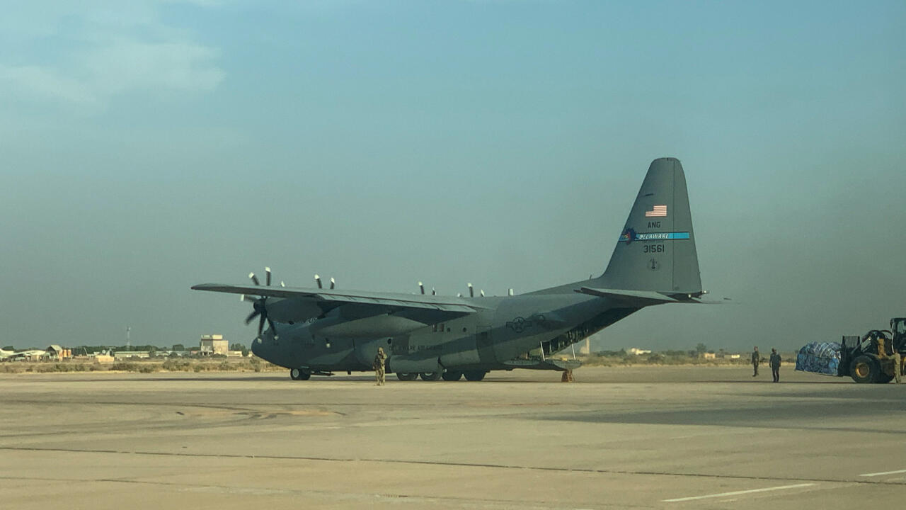 A large military transport aircraft sits on an airport tarmac as several people stand nearby.