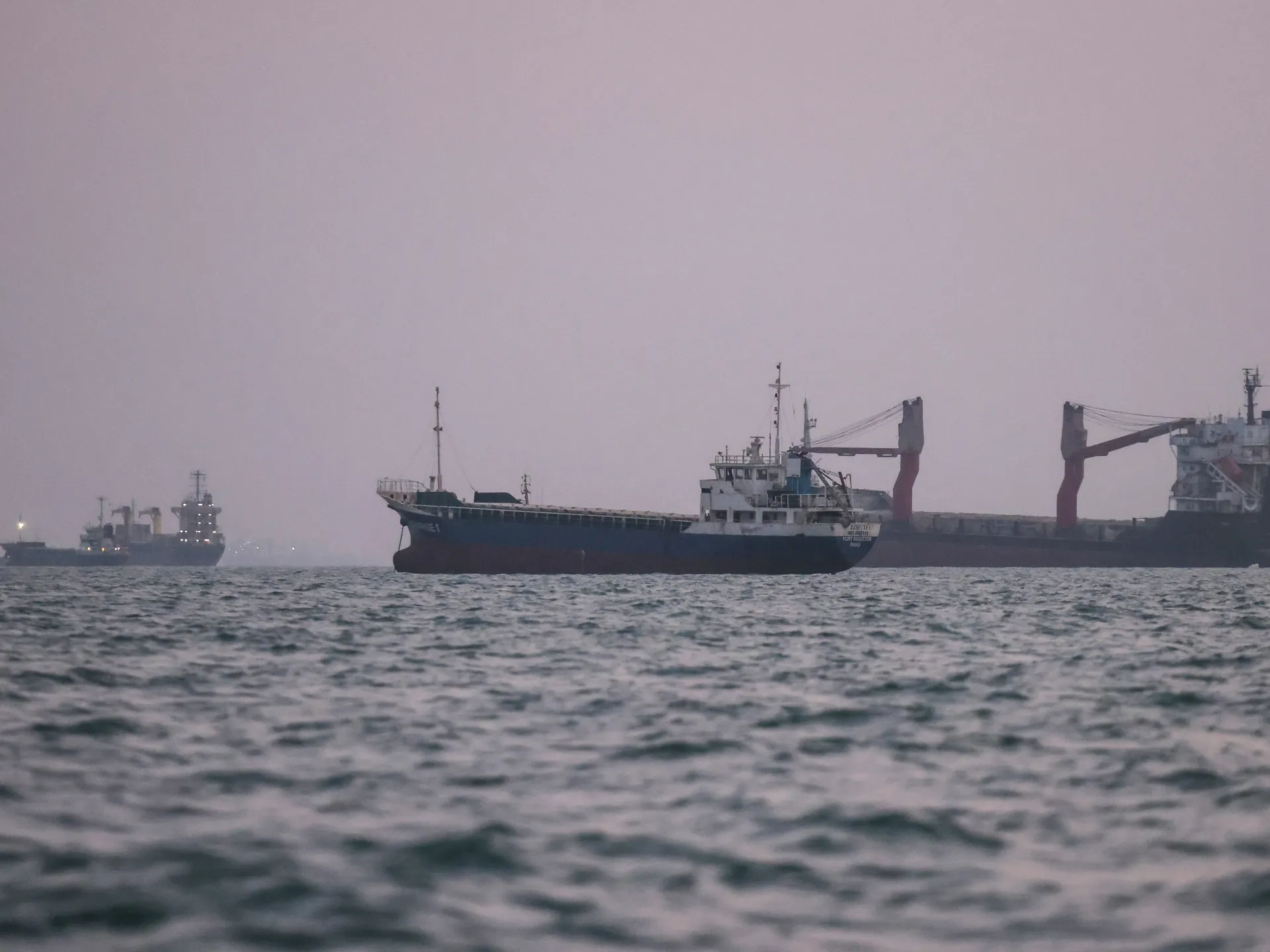 Cargo ships sail across choppy waters beneath a hazy sky.
