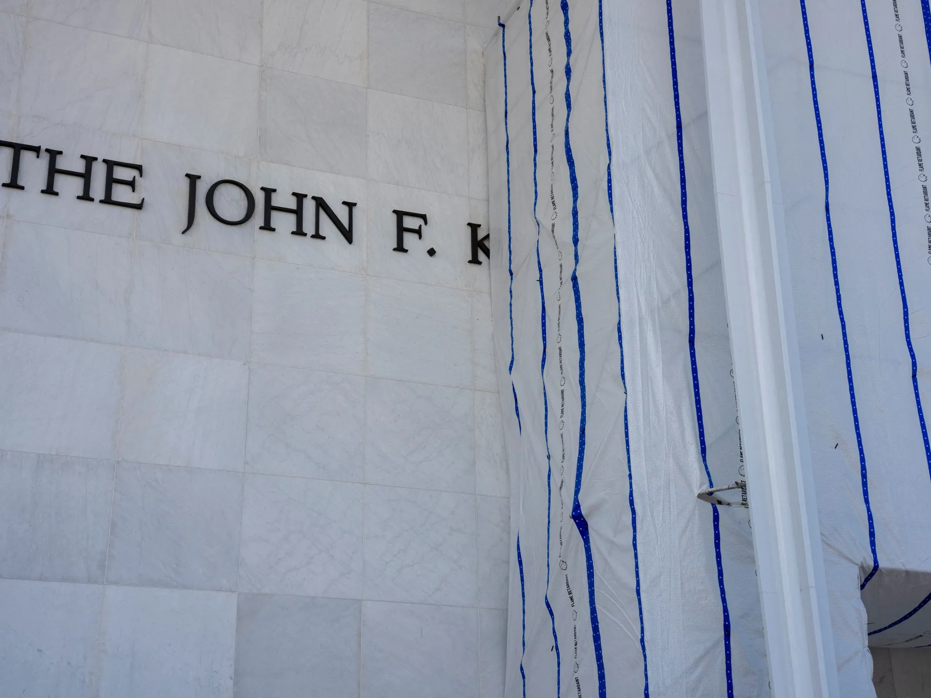 Partial John F. Kennedy Center lettering beside a section covered in protective construction sheeting.