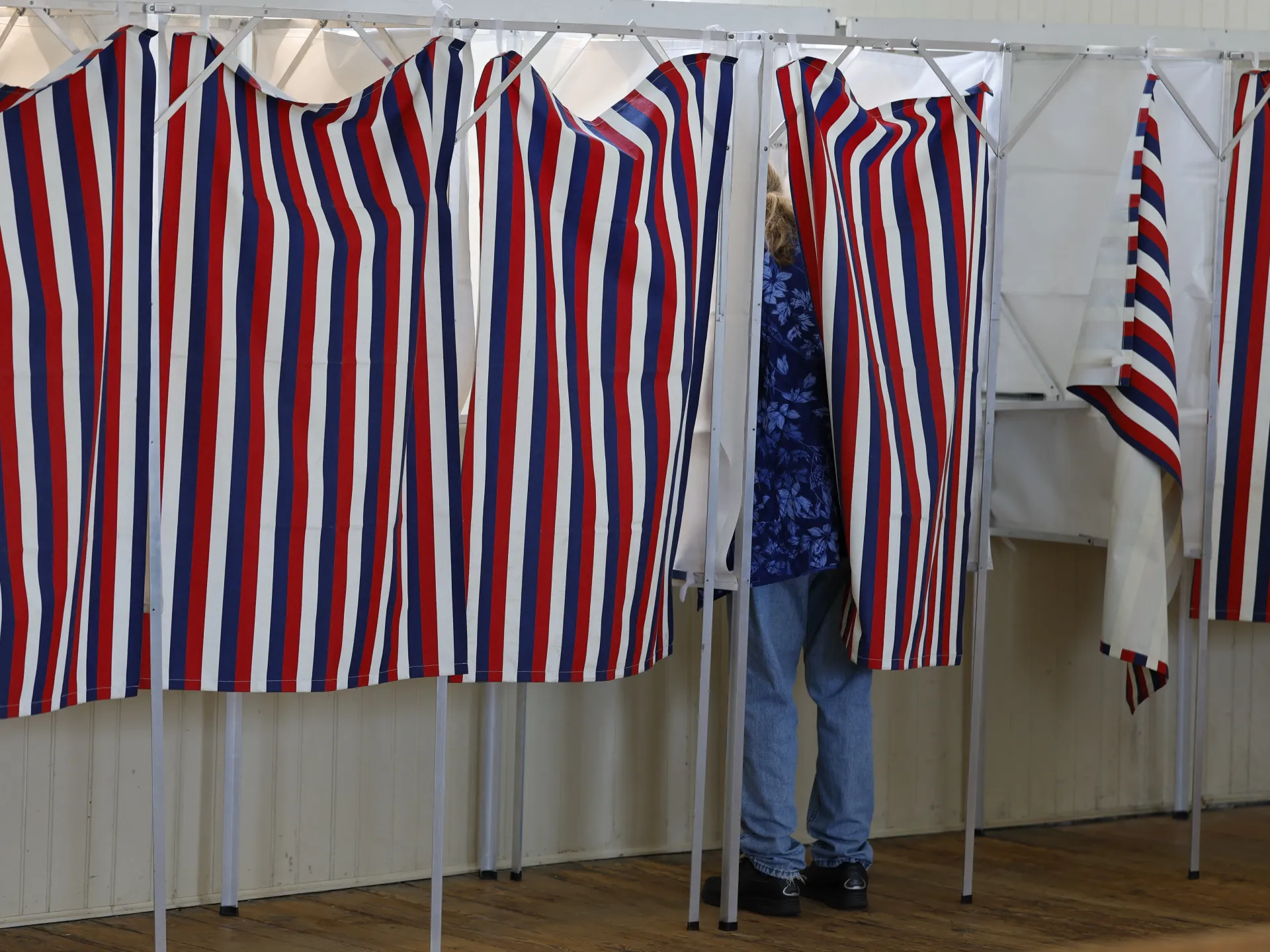 Red, white and blue striped voting booths with a voter partially visible behind curtains