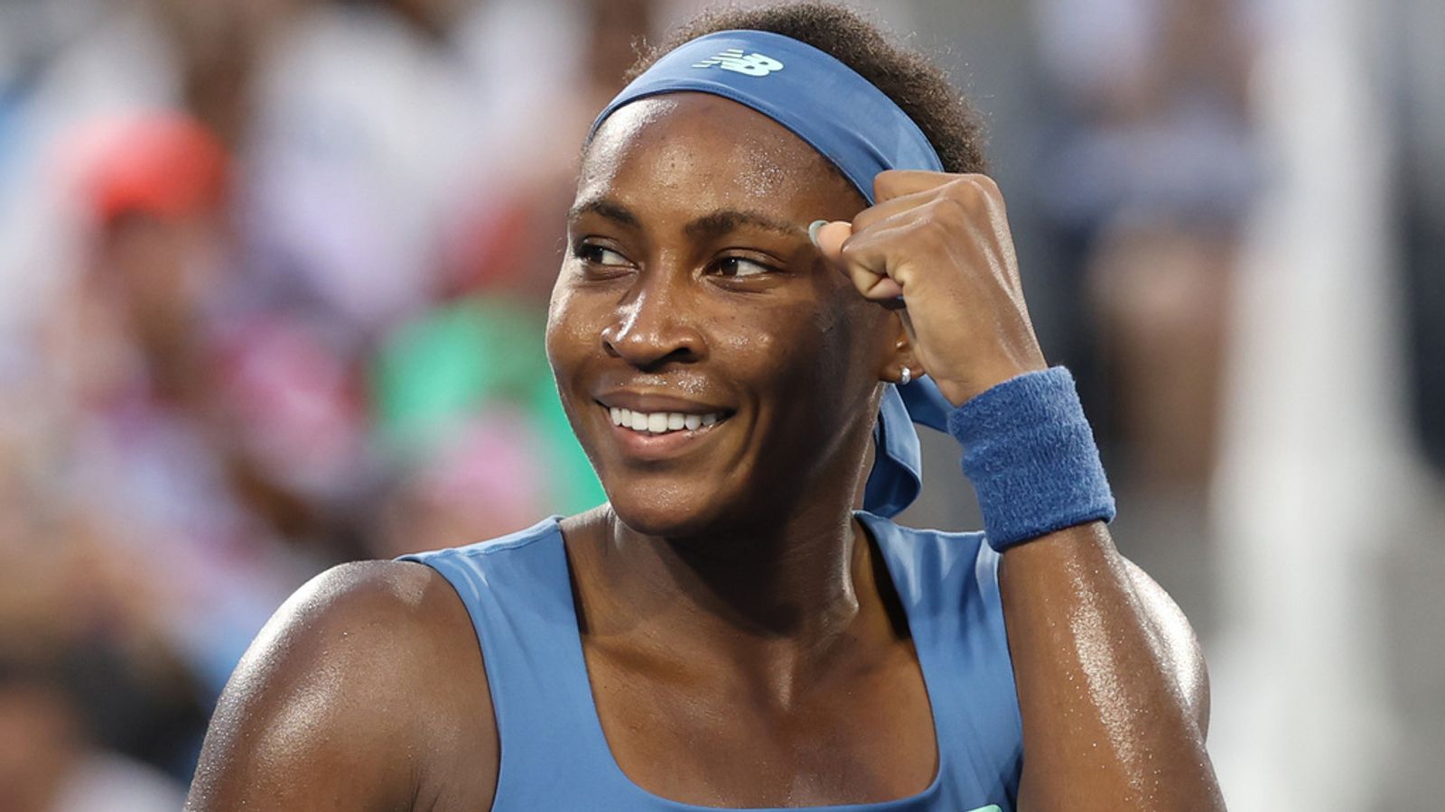 Smiling tennis player in blue outfit and headband raises a clenched fist during a match.